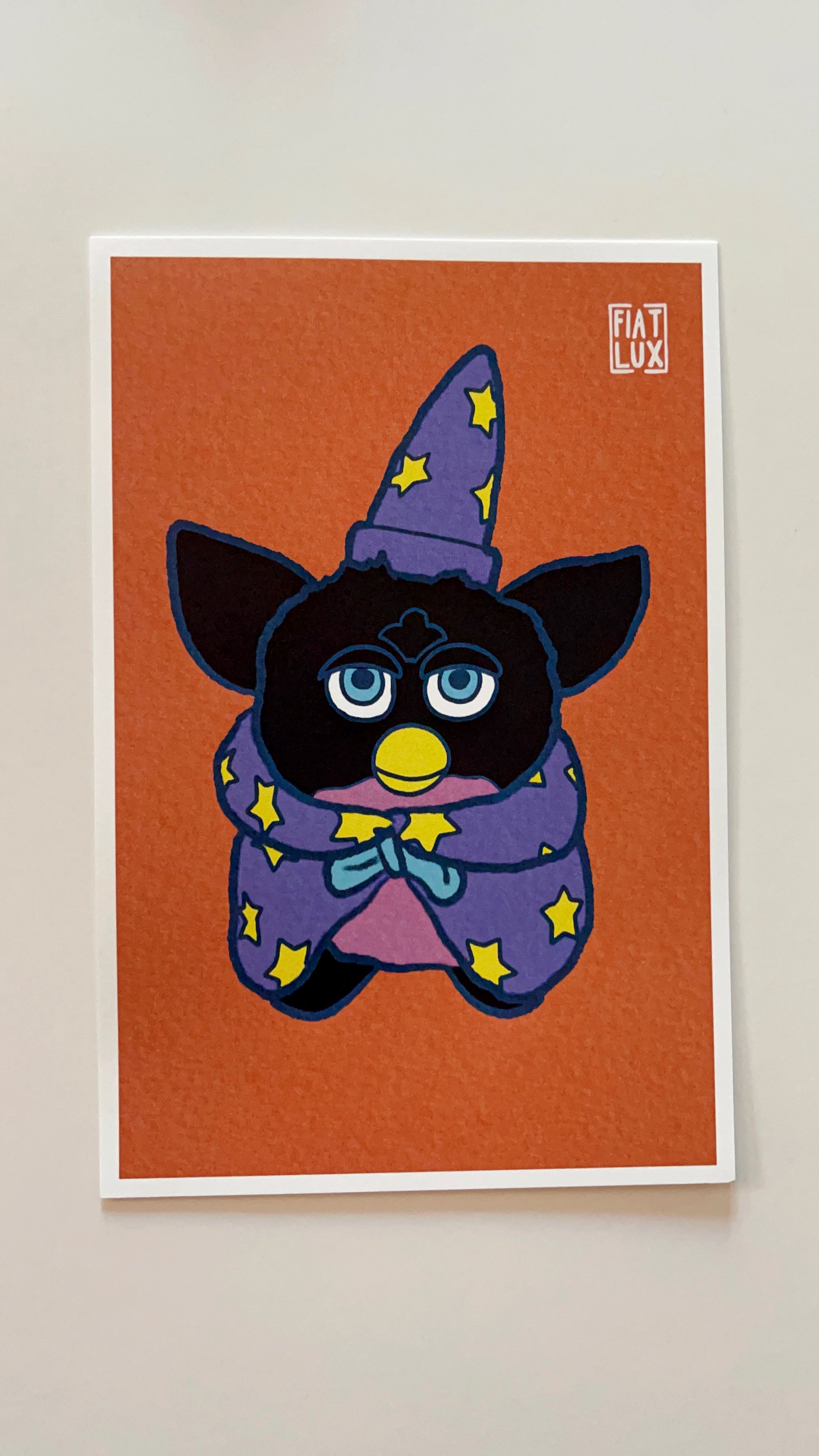 Art print of a furby in a purple wizard hat and cape with yellow stars on a solid orange background.