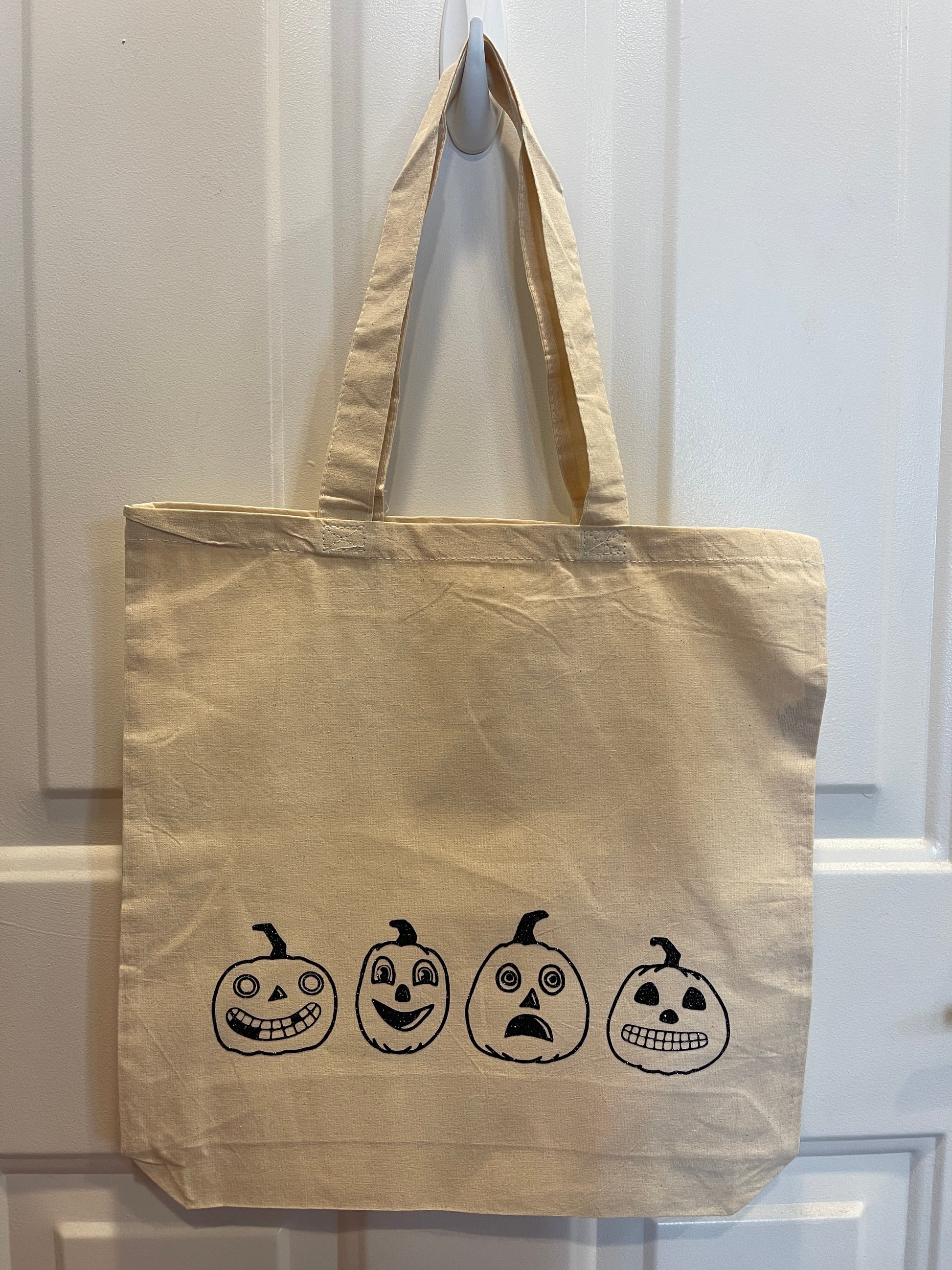 Canvas tote bag with four different pumpkins with vintage inspired faces design in black