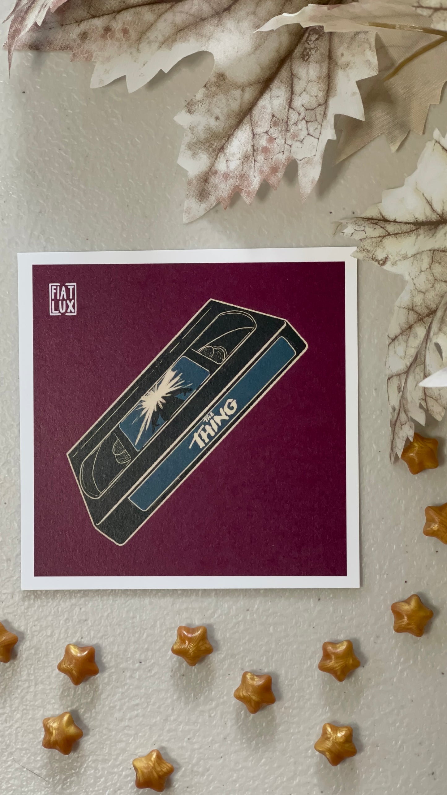Art print of a blue VHS tape of The Thing on a solid burgundy background.