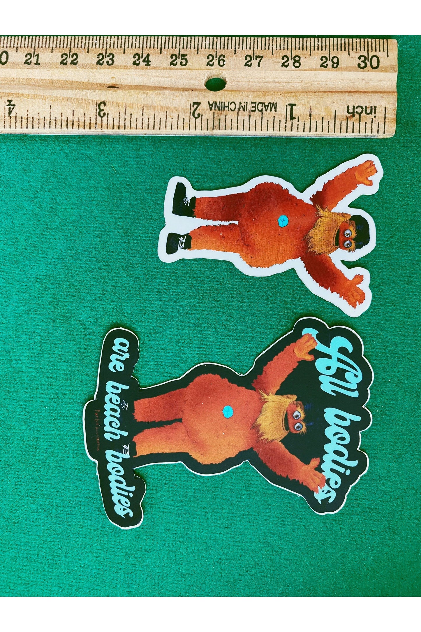 Vinyl stickers of hockey team the flyers mascot gritty. gritty is a large orange furry mascot with googly eyes and an outie belly button. gritty is streaking with only shoes on. one sticker has the phase all bodies are beach bodies in blue cursive.