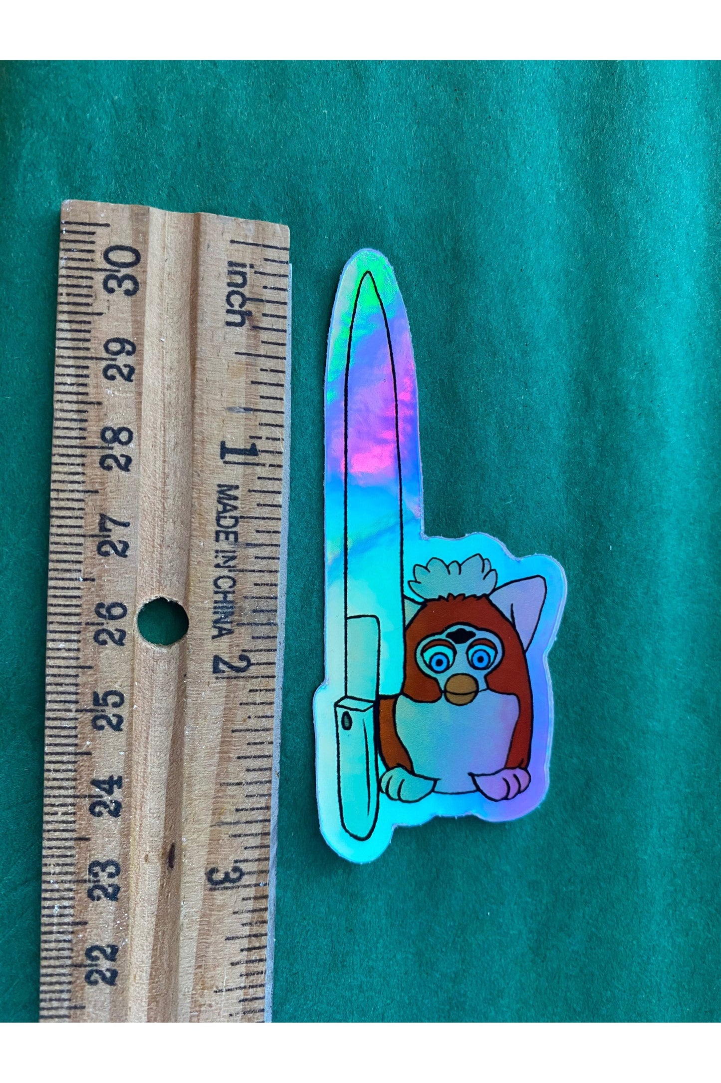 vinyl holographic sticker of a red toned furby with a large knife