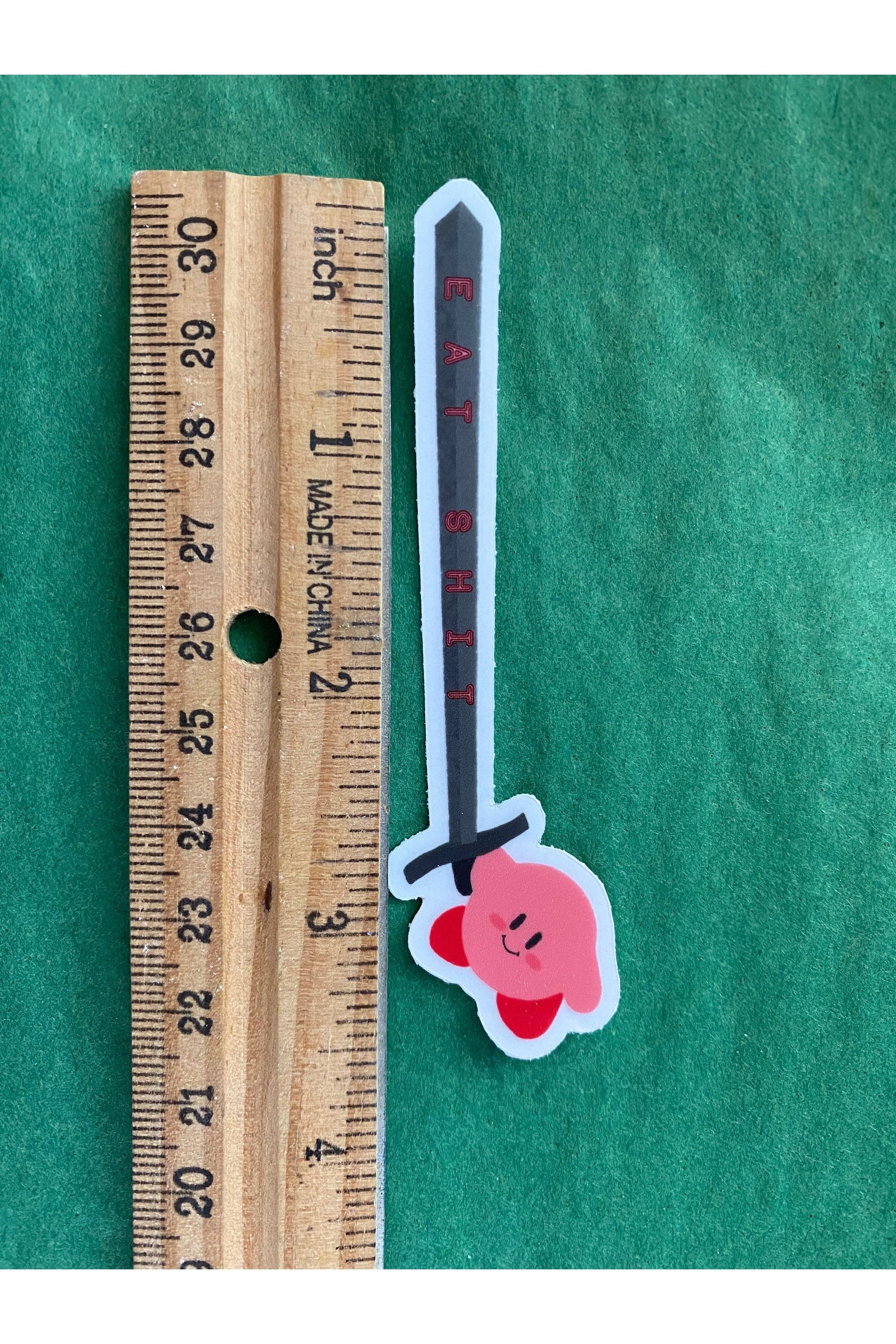 vinyl sticker of kirby holding a sword that reads eat shit in pink text down the blade